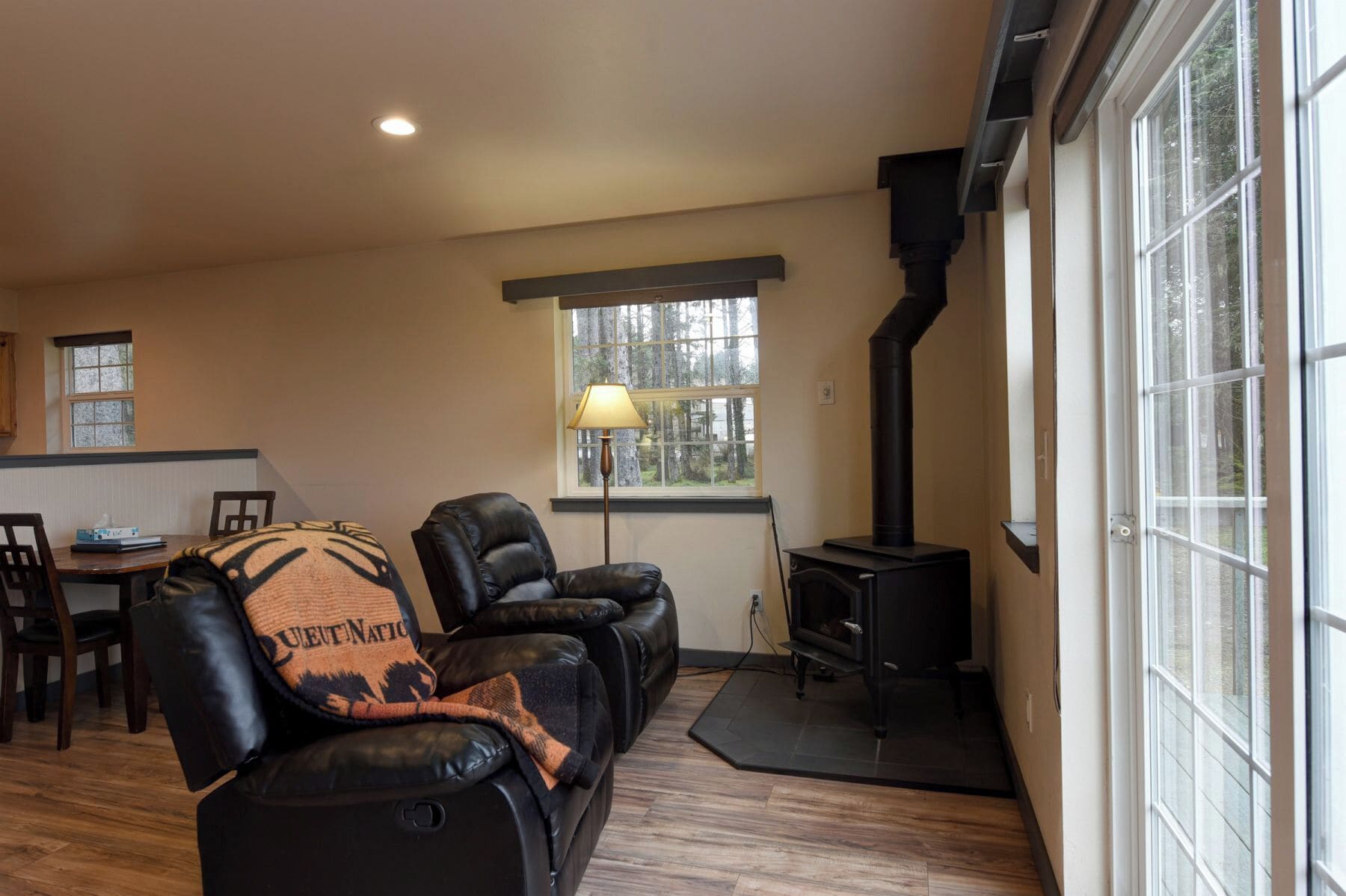A cozy living room with a fireplace, leather sofas, a dining area, and large windows.