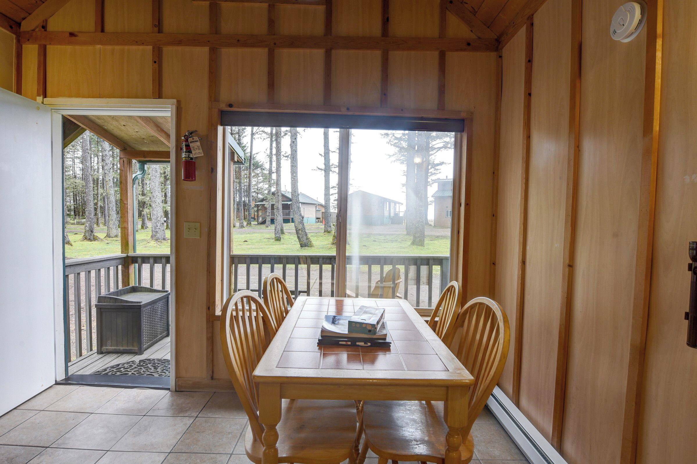 A wooden cabin with a dining table and chairs, a view of the forest, and a fire extinguisher on the wall.