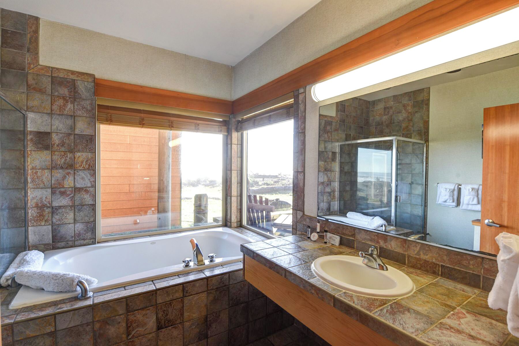 A modern bathroom with a large bathtub, a sink, and a shower. There is a large window providing a view of the outdoors.