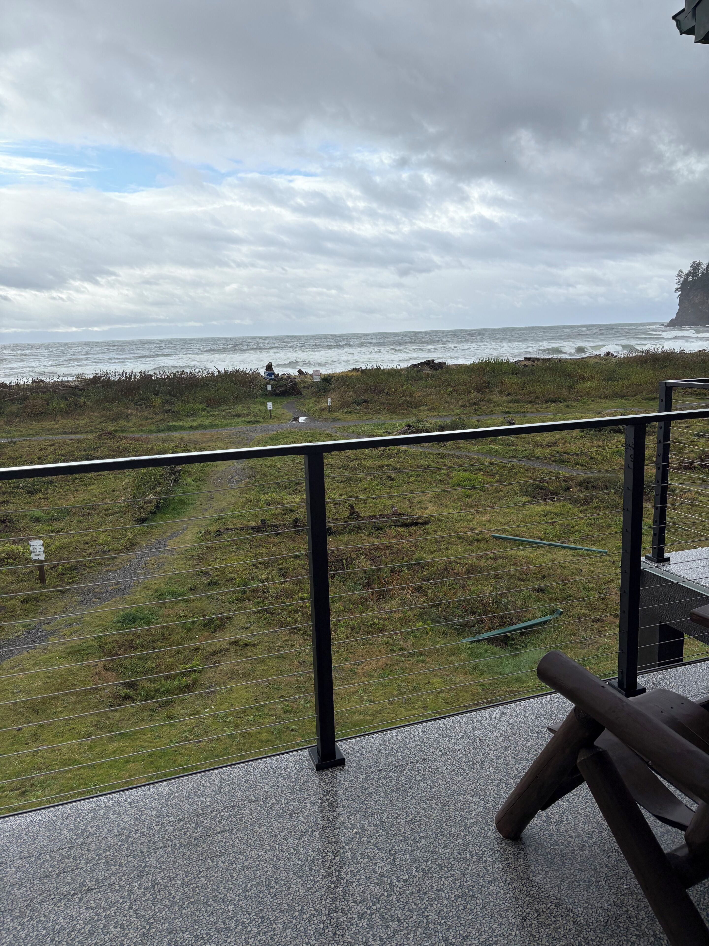 A balcony with a view of the sea and a grassy path leading to a cliff.
