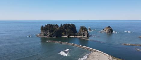 A coastal landscape with a rocky island, clear blue sky, and calm sea.