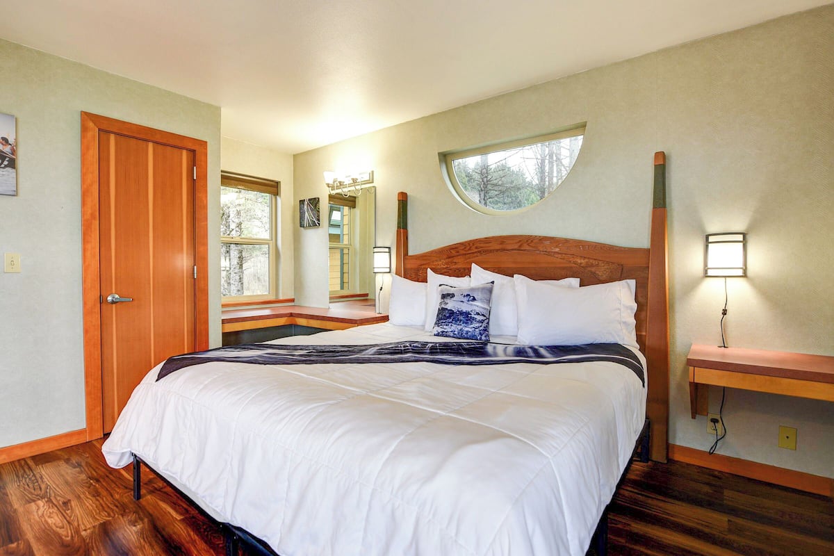 A bedroom with a large bed, a wooden headboard, a nightstand with a lamp, a window, and a door.