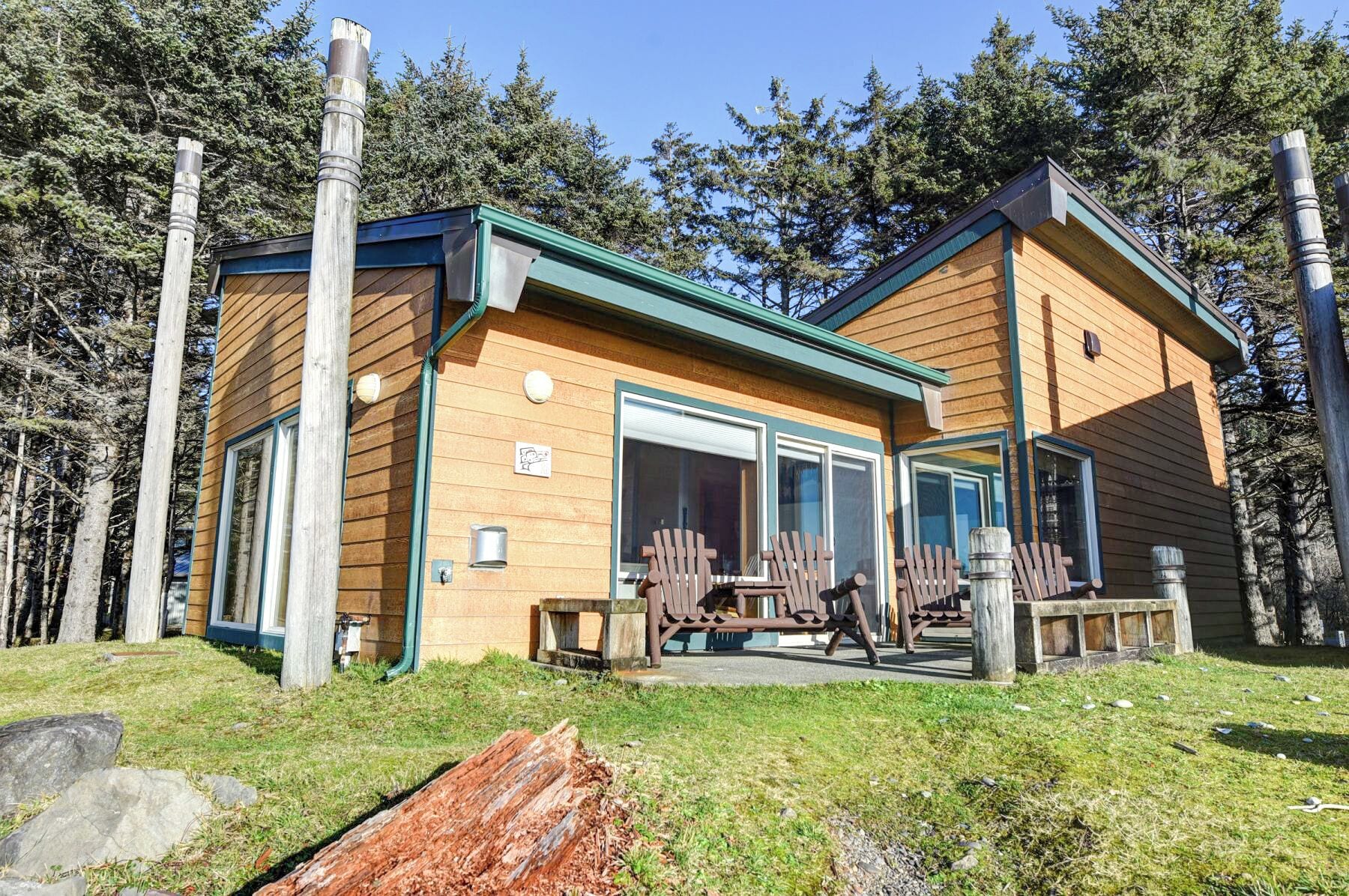 Eine Holzhütte mit grüner Dachdeckung, großen Fenstern und zwei Adirondack-Stühlen vor der Tür.