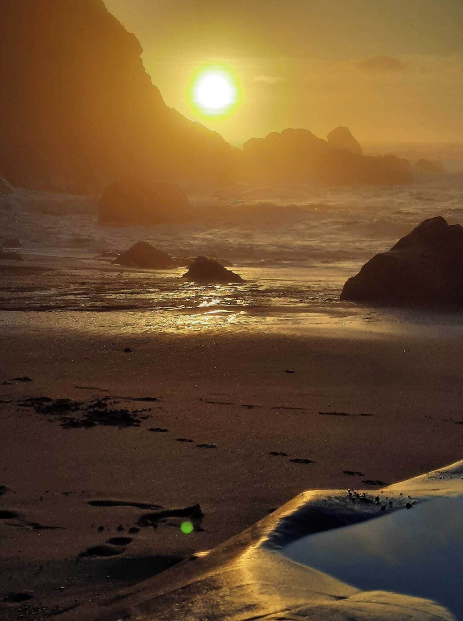 A beach with rocks and the sun setting in the background.