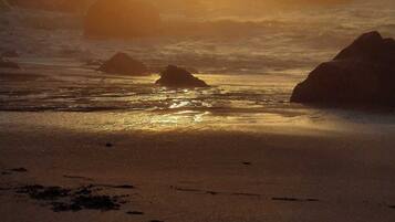 A beach with rocks and the sun setting in the background.