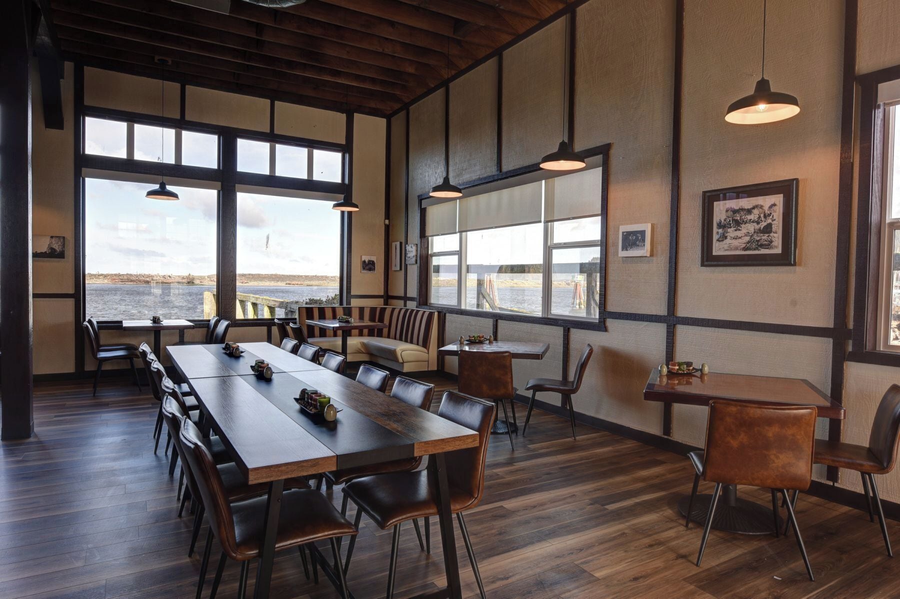 A spacious dining area with a long wooden table, multiple chairs, and large windows offering a view of the water.