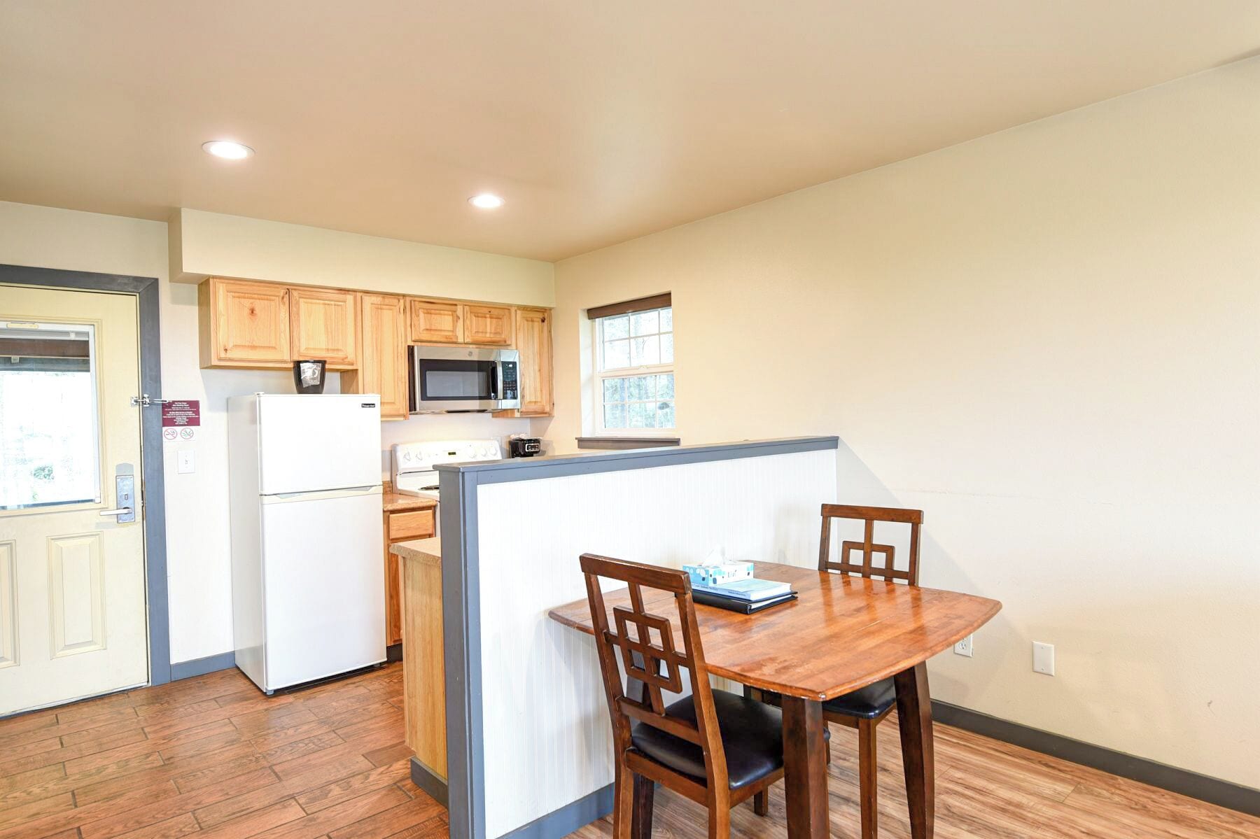 A compact kitchen with wooden cabinets, a microwave, a refrigerator, and a dining table with chairs.