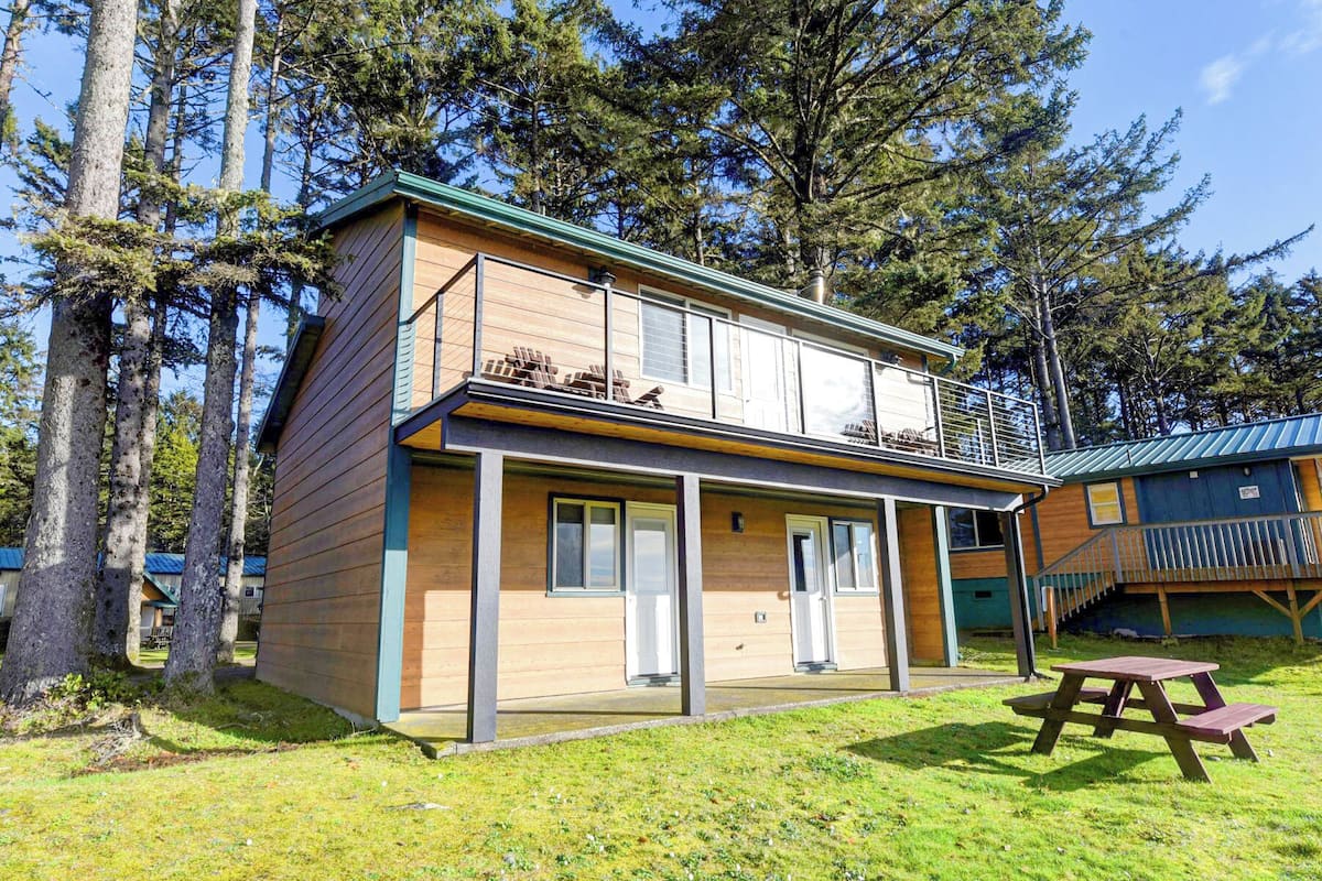 A two-story cabin with a balcony, a covered porch, and a picnic table in the yard.