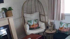 A living room with a wicker chair, a sofa, a small table with a lamp, and a fireplace. - 2 Bed Chalet Sleeps 5 - Pets, Parking, Near Beach (Great Yarmouth)