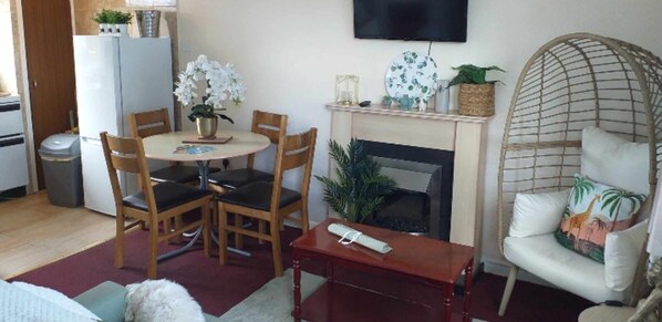 A living room with a round table, chairs, a sofa, a TV mounted on the wall, and a fireplace. - 2 Bed Chalet Sleeps 5 - Pets, Parking, Near Beach (Great Yarmouth)