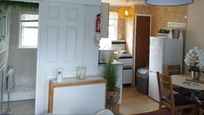 A compact kitchen with white cabinets, a wooden table, and chairs. There is a refrigerator, a washing machine, and a small dining area with a table and chairs. - 2 Bed Chalet Sleeps 5 - Pets, Parking, Near Beach (Great Yarmouth)