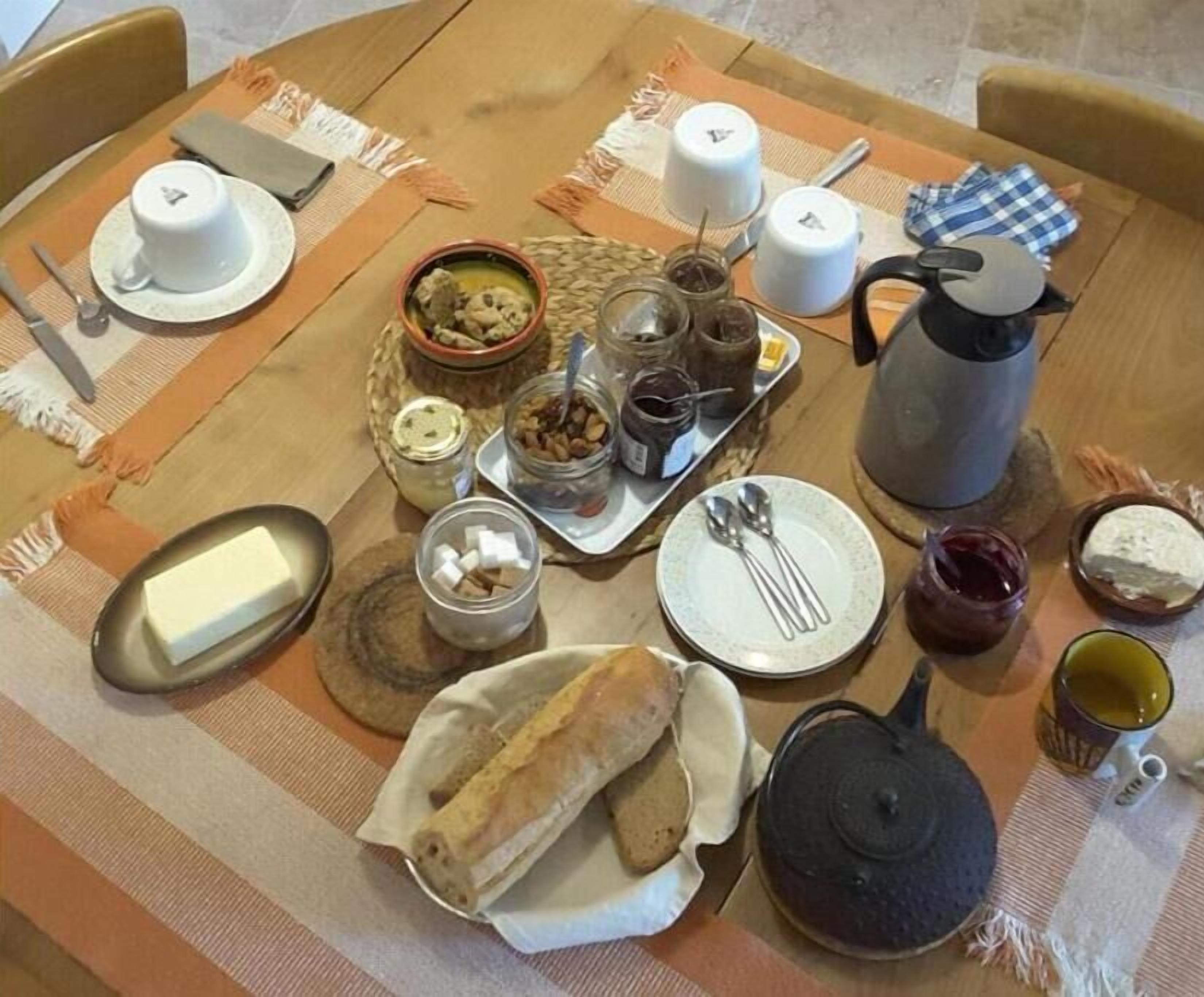 Une table mise pour le petit-déjeuner, avec une variété d’aliments, notamment du pain, du beurre, des confitures et une théière.