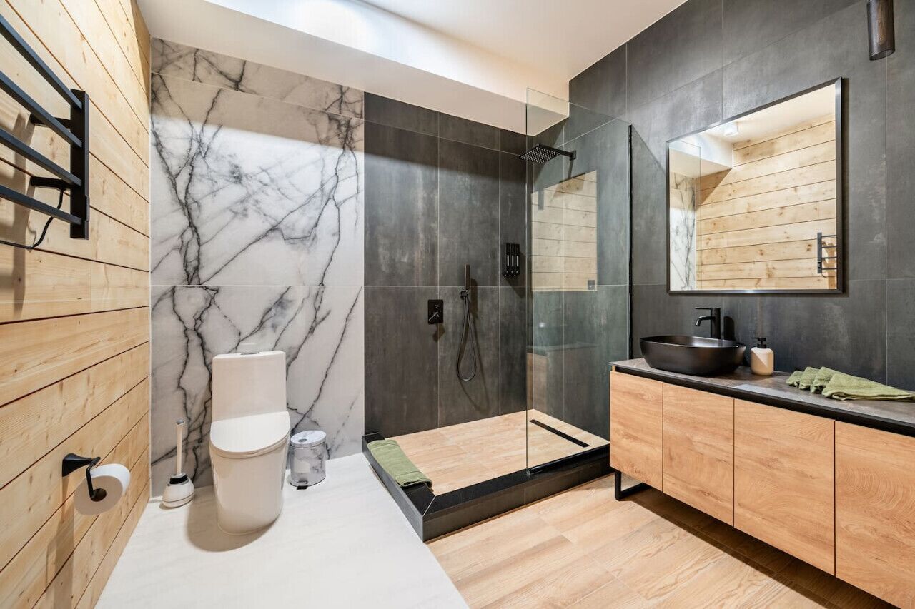 A modern bathroom with a marble wall, a wooden vanity, a large mirror, and a shower area.