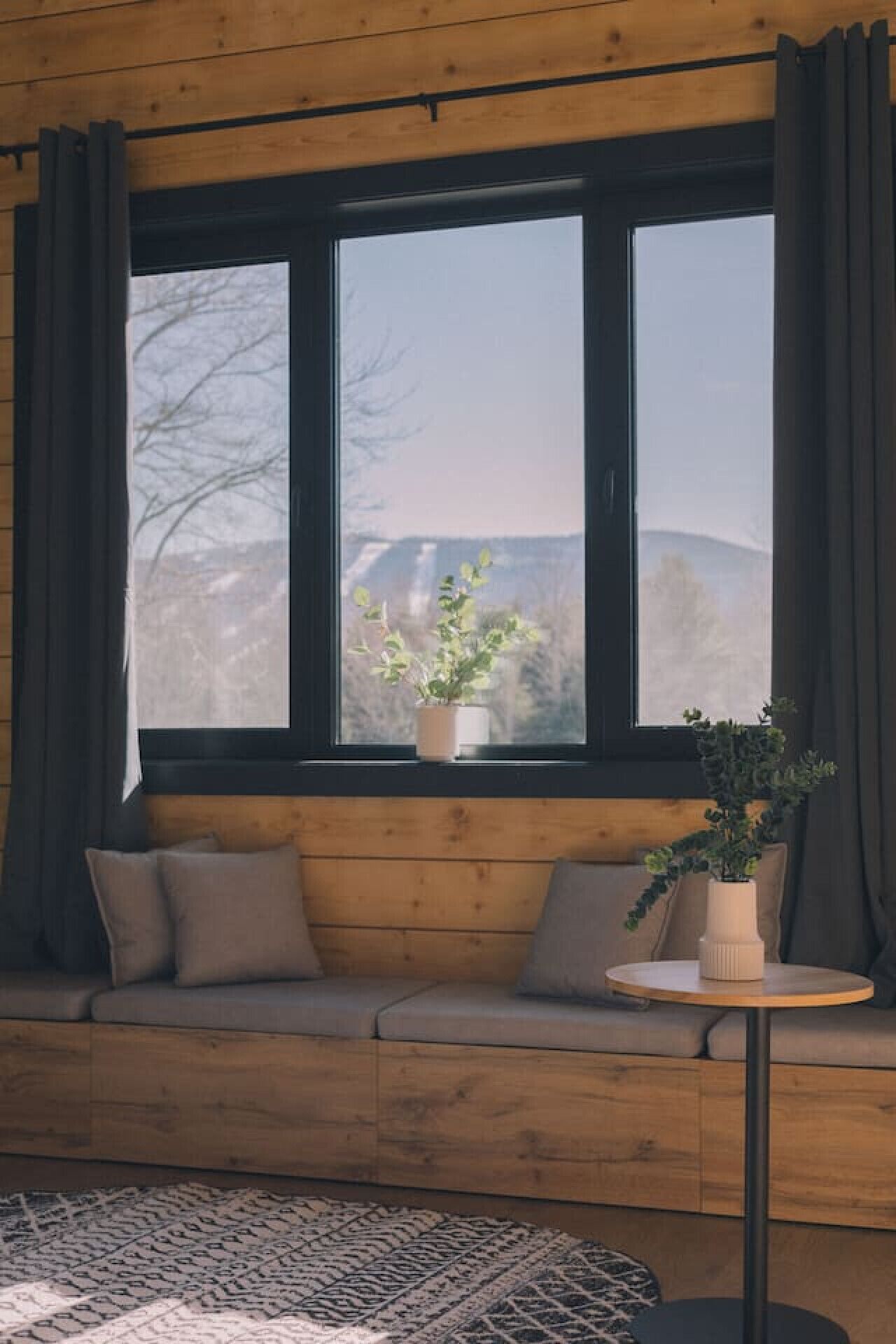 Ein gemütliches Zimmer mit einer hölzernen Sitzbank, einem runden Tisch und einem großen Fenster mit Vorhängen.