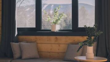 Ein gemütliches Zimmer mit einer hölzernen Sitzbank, einem runden Tisch und einem großen Fenster mit Vorhängen.