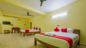 Habitación de hotel con dos camas individuales, suelo de madera, ventilador de techo, televisor montado en la pared y una pequeña mesa con sillas.
