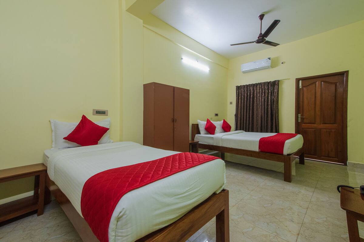 A hotel room with two beds, a wardrobe, an air conditioning unit, and a ceiling fan.