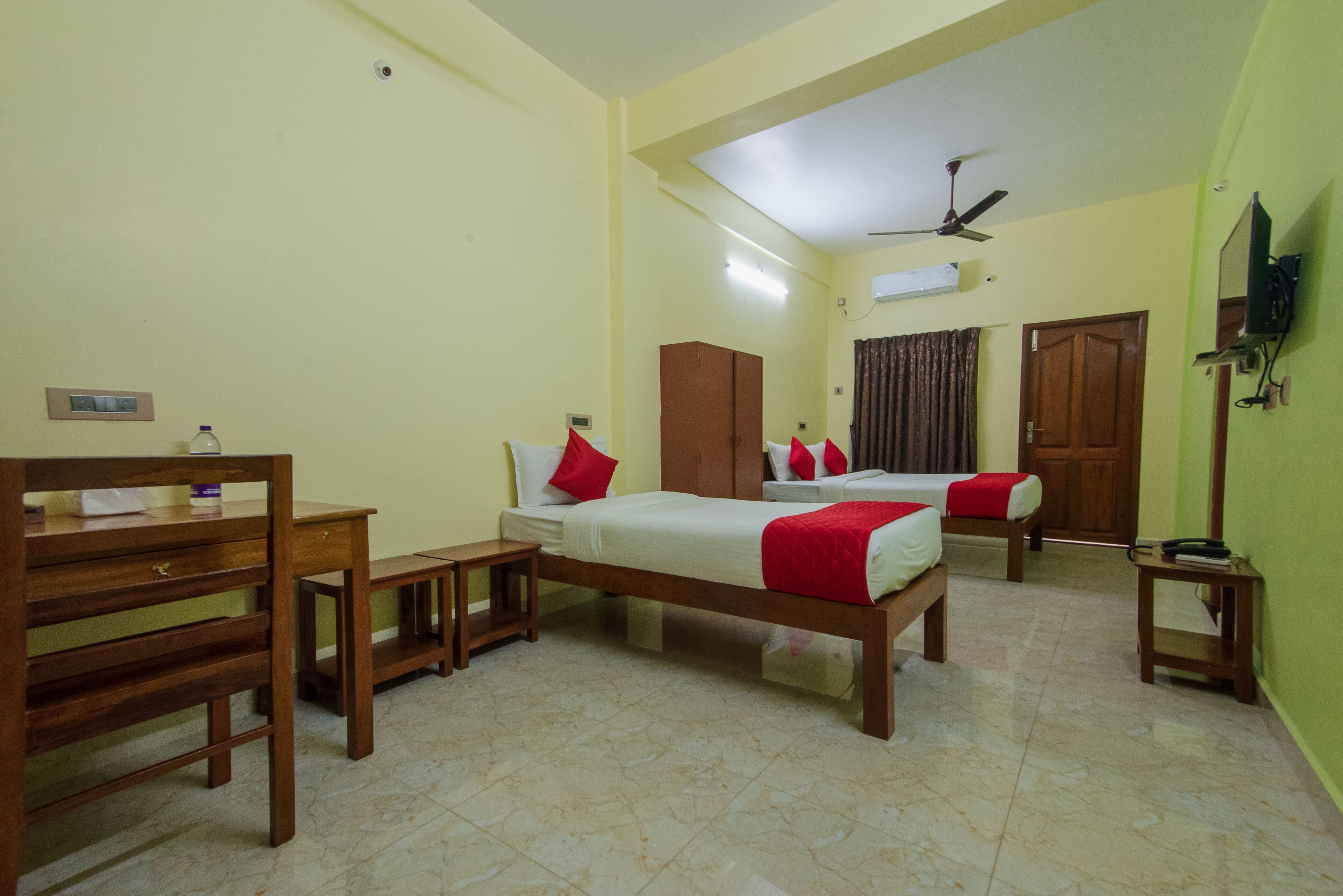 A hotel room with two beds, a desk, a chair, a ceiling fan, and a TV mounted on the wall.