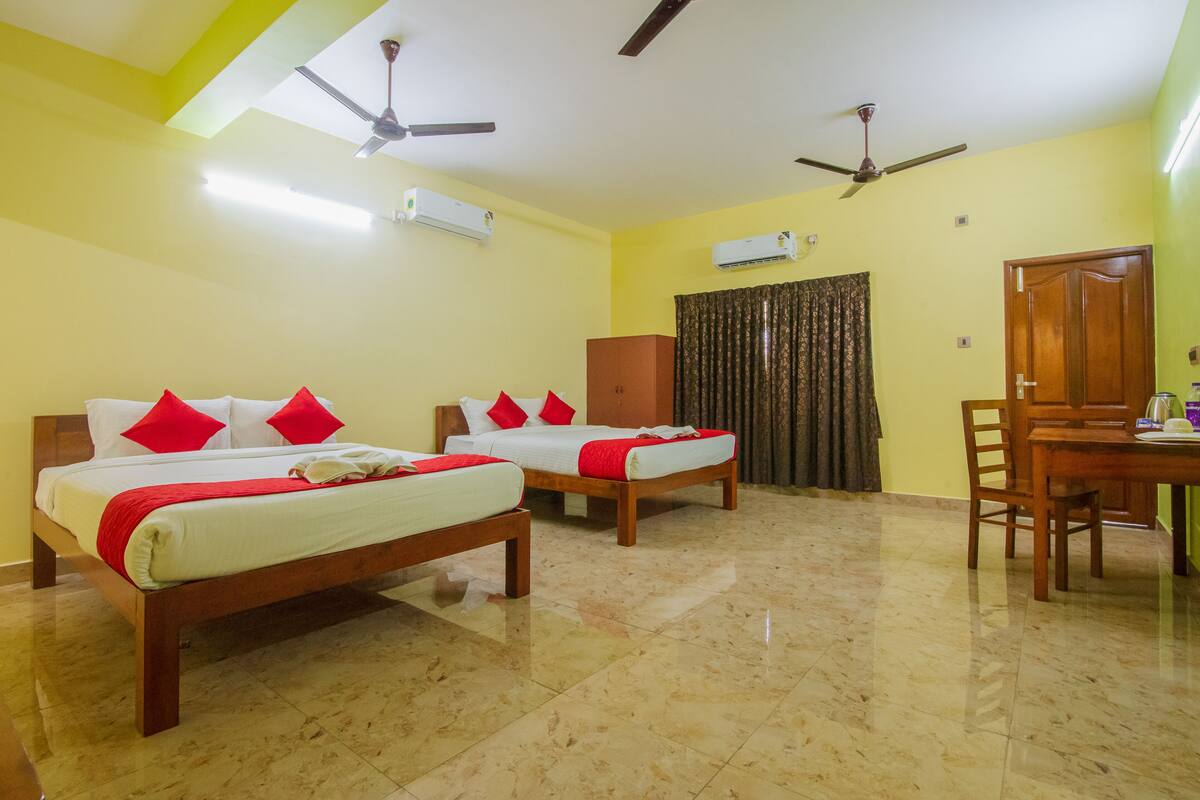 A hotel room with two wooden beds, red pillows, a wooden table, and ceiling fans.