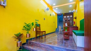 Un hall de hotel con una pared amarilla, una recepción, una escalera y una zona de estar verde.
