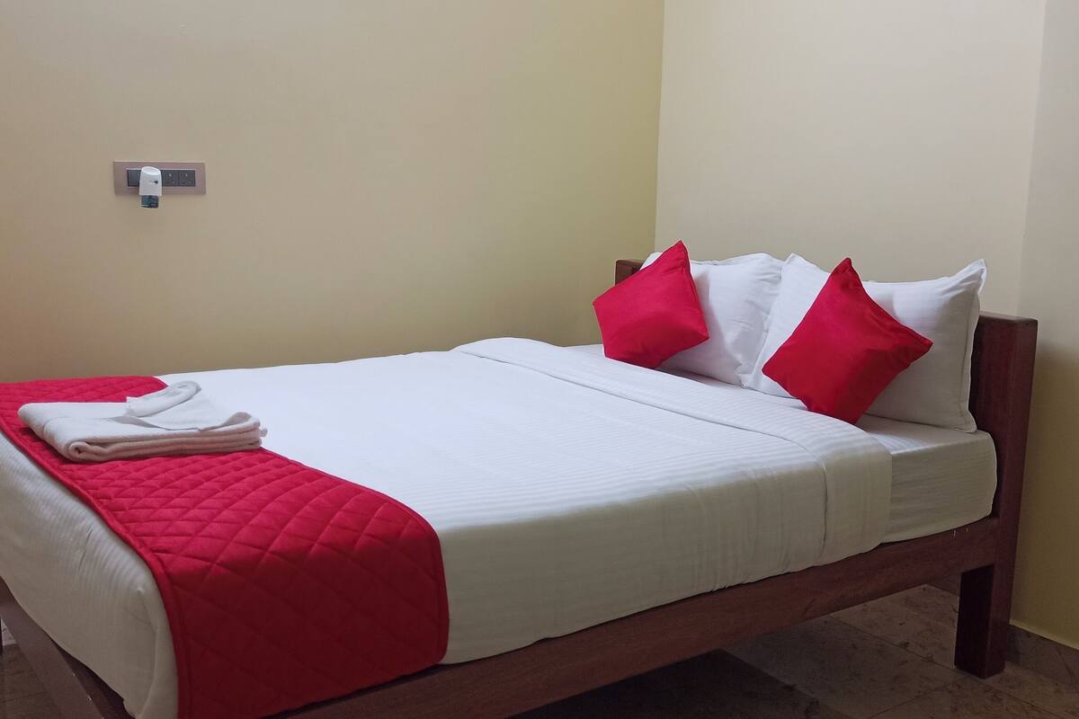 A neatly made bed with white and red bedding, a red quilted throw, and a folded white towel on the left side.