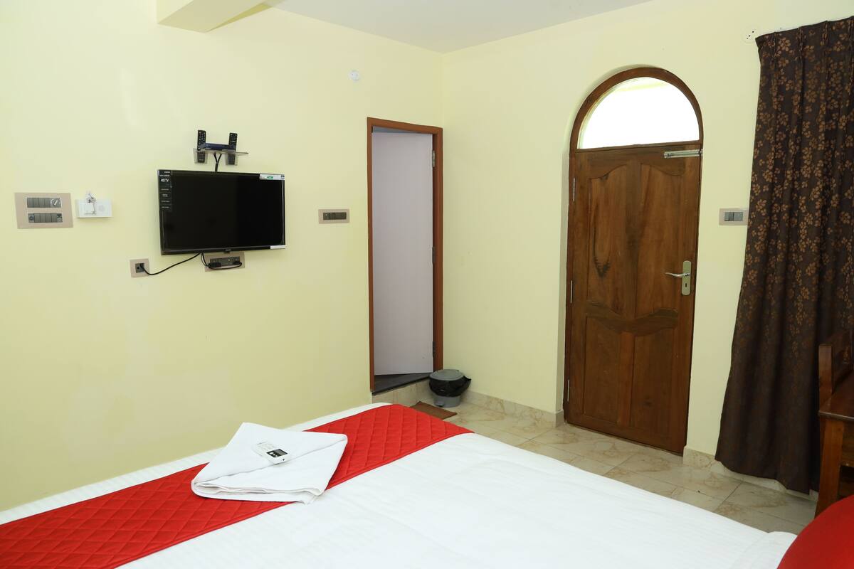 A hotel room with a bed, a TV mounted on the wall, a wooden door, and a curtain.