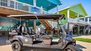 A golf cart parked in front of a building with a blue and green color scheme, a sign reading "Wait 'n Sea", and a wooden staircase leading to a balcony. - `Enjoy the Sun in Your Private Pool, Charcoal Grill & Fire Pit for Cozy Evenings – Free Golf Cart, Private Pool, Just Steps from the Beach!` (Port Aransas)
