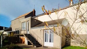 Ein zweistöckiges Haus mit einer Treppe zum Obergeschoss, einer kleinen Veranda und einem Garten.