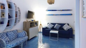 A compact living space with a sofa, a small coffee table, a bookshelf, a television, and a wall-mounted shelf. - B&B Angelica - Apartment (Bacoli)