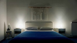 A bedroom with a large bed, two bedside tables, a wall hanging, and a radiator. - B&B Angelica - Apartment (Bacoli)