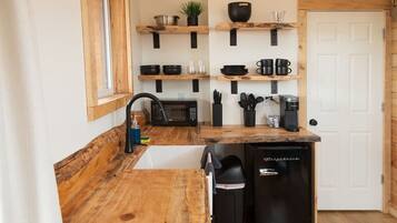 A compact kitchen with wooden countertops, a sink, a microwave, and a coffee maker.