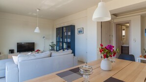 A modern living room with a sofa, a dining table with a vase of flowers, and a bookshelf. - Appartment At Heraklion, Crete, Greece. Kokkini Hani, Brachokipos (heraklion)