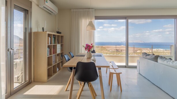 A modern living room with a dining area, a bookshelf, and a large window with a view of the sea. - Appartment At Heraklion, Crete, Greece. Kokkini Hani, Brachokipos (heraklion)
