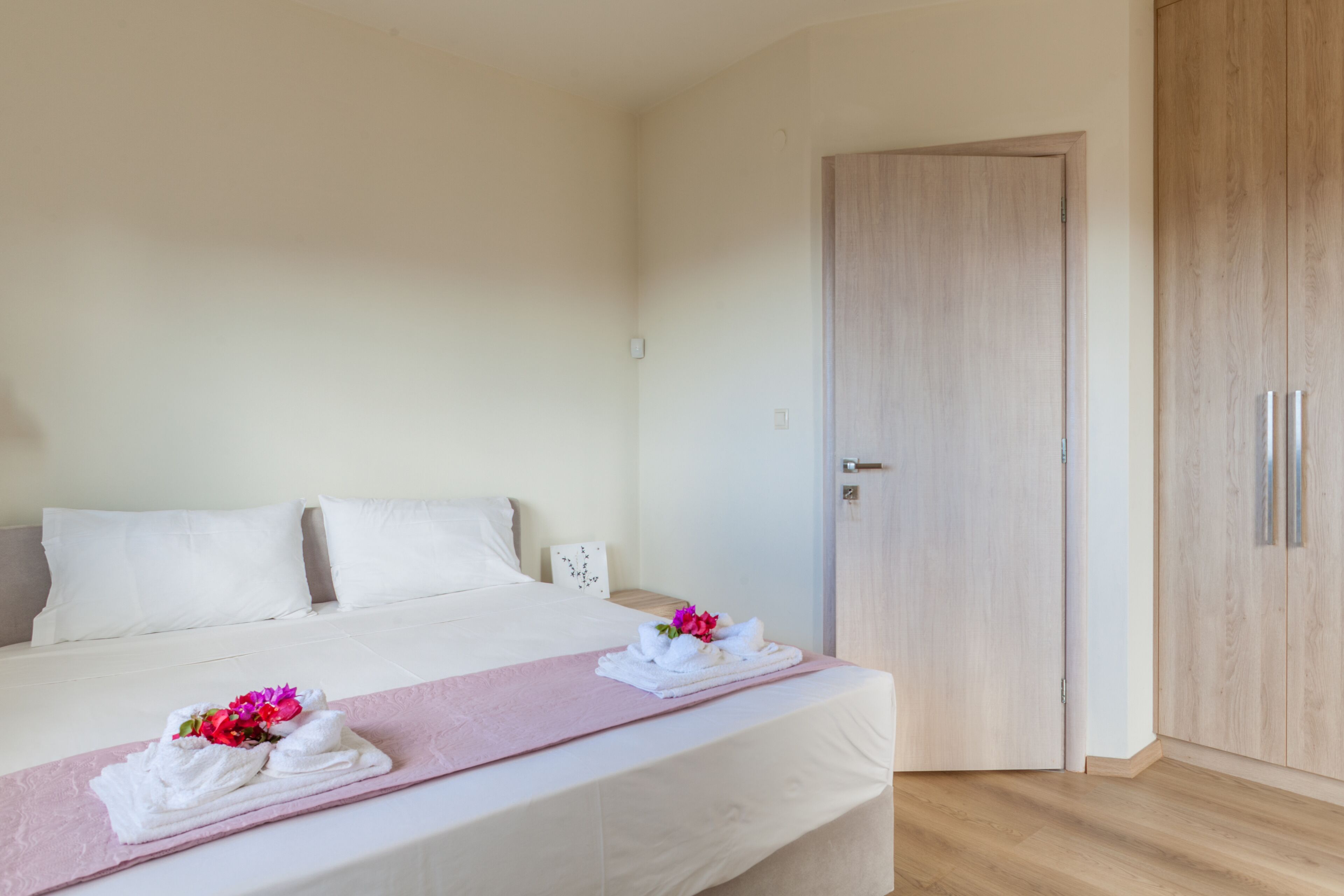 A hotel room with a bed, a wooden wardrobe, and a pink towel on the bed.