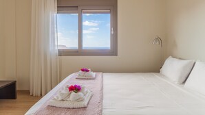 A hotel room with a large bed, a bedside table, a window with curtains, and a view of the sky. - Appartment At Heraklion, Crete, Greece. Kokkini Hani, Brachokipos (heraklion)