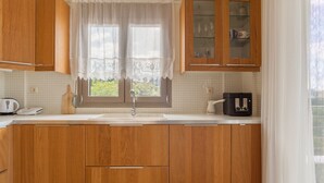 A kitchen with wooden cabinets, a window with lace curtains, a sink, and a coffee maker. - Appartment At Heraklion, Crete, Greece. Kokkini Hani, Brachokipos (heraklion)