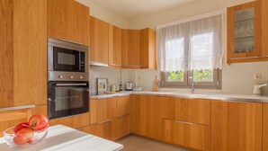 A kitchen with wooden cabinets, a microwave, an oven, a sink, and a window with curtains. - Appartment At Heraklion, Crete, Greece. Kokkini Hani, Brachokipos (heraklion)