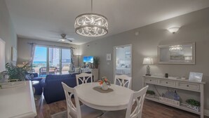 Ein modernes Wohnzimmer mit einem runden weißen Tisch, weißen Stühlen, einem Deckenventilator und Blick auf den Balkon.