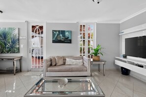 A modern living room with a sofa, coffee table, TV, and artwork. - Massive 3 bedroom with Pool (Palmas del Mar)