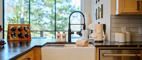 A modern kitchen with a built-in sink, wooden cabinets, a wine rack, and a view of trees through a large window.