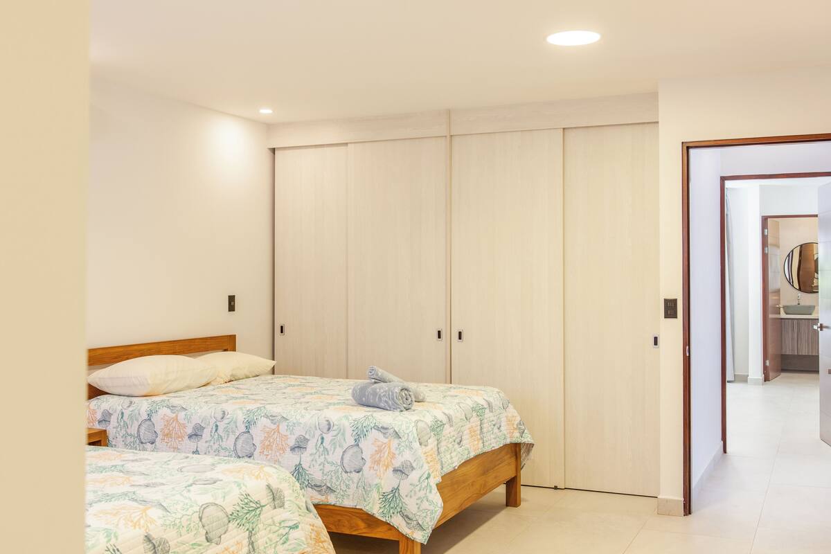 Ein Schlafzimmer mit zwei Betten, einem Kleiderschrank und einem durch eine geöffnete Tür einsehbaren Badezimmer.