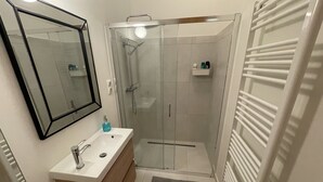 Un baño moderno con ducha de vidrio, un lavabo blanco con espejo y un perchero para toallas.