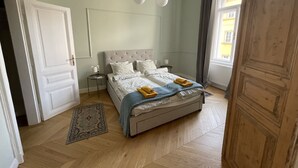 Un dormitorio con cama, mesitas de noche, alfombra y ventana con cortinas.