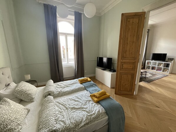 A bedroom with a bed, a TV, a bookshelf, and a door leading to another room.