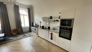 Una cocina moderna con armarios blancos, piso de madera en patrón de espiga, horno empotrado y un comedor con una silla y mesa.