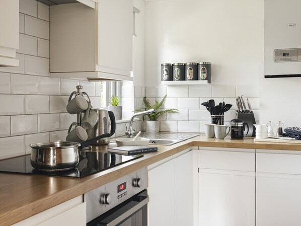 A modern kitchen with white cabinetry, stainless steel appliances, and a wooden countertop.