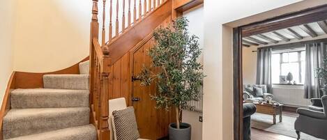 Una escalera con barandillas de madera, una planta en maceta, una silla y vista a un salón con sofá y mesa de centro.