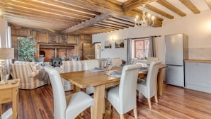 Une cuisine moderne avec des poutres en bois, un coin repas avec des chaises blanches et une cheminée en briques.