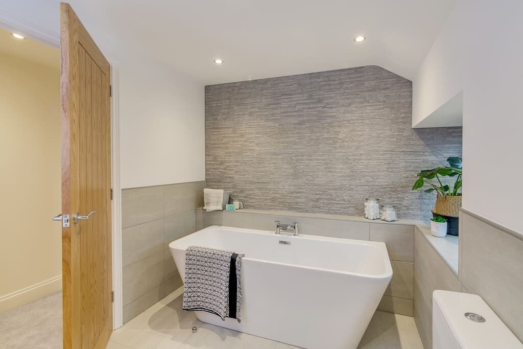 Une salle de bain moderne avec une baignoire sur pieds, une porte en bois et un mur recouvert de carreaux gris.