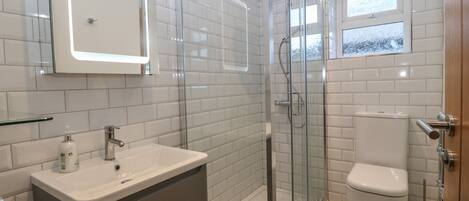 Een moderne badkamer met een douchecabine van glas, een witte wastafel met spiegel en een toilet met een vloertegelpatroon.